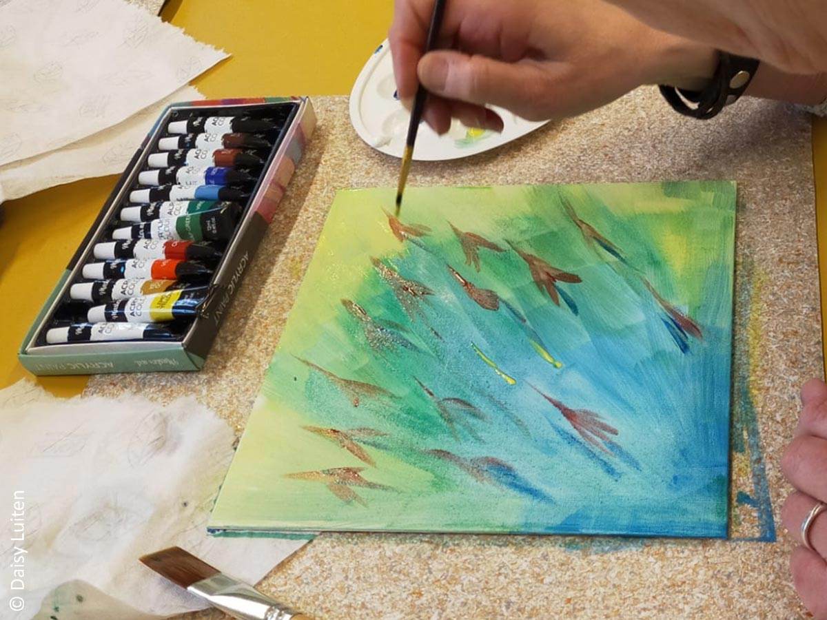 Iemand schildert rode penseelstreken op een blauw, groen, geel geschilderde achtergrond n.a.v. vragen uit de tool Ons Bestaan Op Een Bordje van ontwikkelaar Daisy Luiten