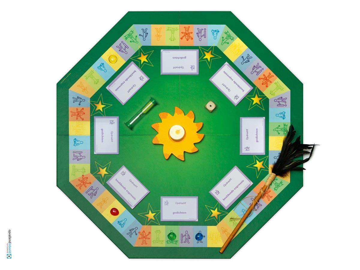 Onderdeel_Ons-Bestaan-Op-Een-Bordje_spelbord_met_houten_zon_praatstok_dobbelsteen_en_tranen-parels_Daisy-Luiten_1200x900 Het groene achthoekige spelbord van Ons Bestaan Op Een Bordje staat uitgestald alsof het gespeeld wordt. Een houten dobbelsteen en een groene zandloper liggen erop. Tranen in de vorm van parels liggen op verschillende plekken van het gekleurde achthoekige traject. Een houten zon met een lichtje erin prijkt in het midden van het spelbord. Aan iedere zijde van de acht kanten van het traject ligt een stapel opdrachtkaarten. En een houten praatstok met zwarte veren ligt deels over het traject.