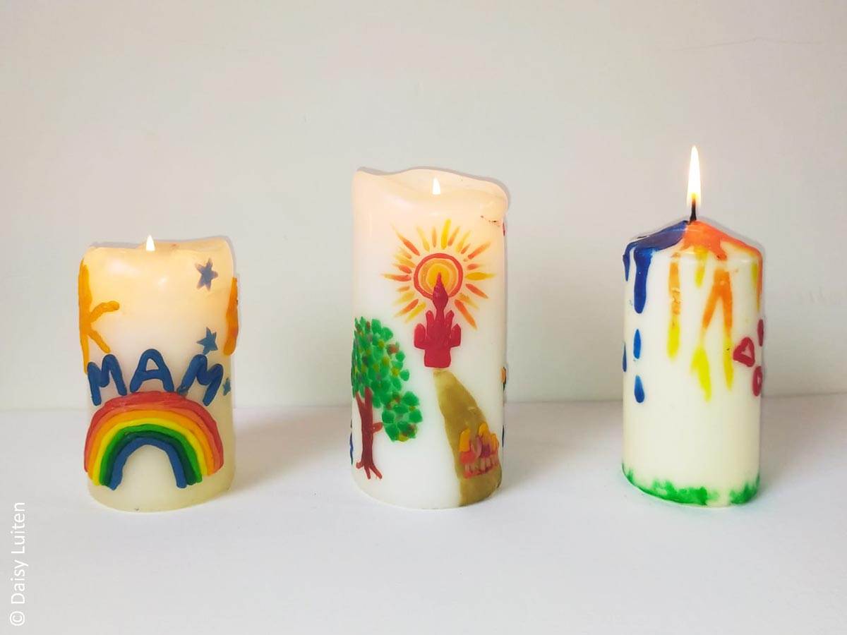 Drie brandende witte kaarsen versierd met gekleurde stukjes kaarsenwas. Op de eerste kaars staat mam op een regenboog erboven hangen blauwe sterren. Op de tweede kaars is een gouden pad zichtbaar met aan het einde een kasteel en aan het begin 3 mensfiguurtjes hand in hand. Links van het pad staat een mooie groene boom. De derde kaars heeft onder groen gras, en van bovenaf lijkt het of in blauw tranen naar beneden druppelen, in het midden zijn dat oranje stralen en rechts zijn rode hartjes gemaakt.